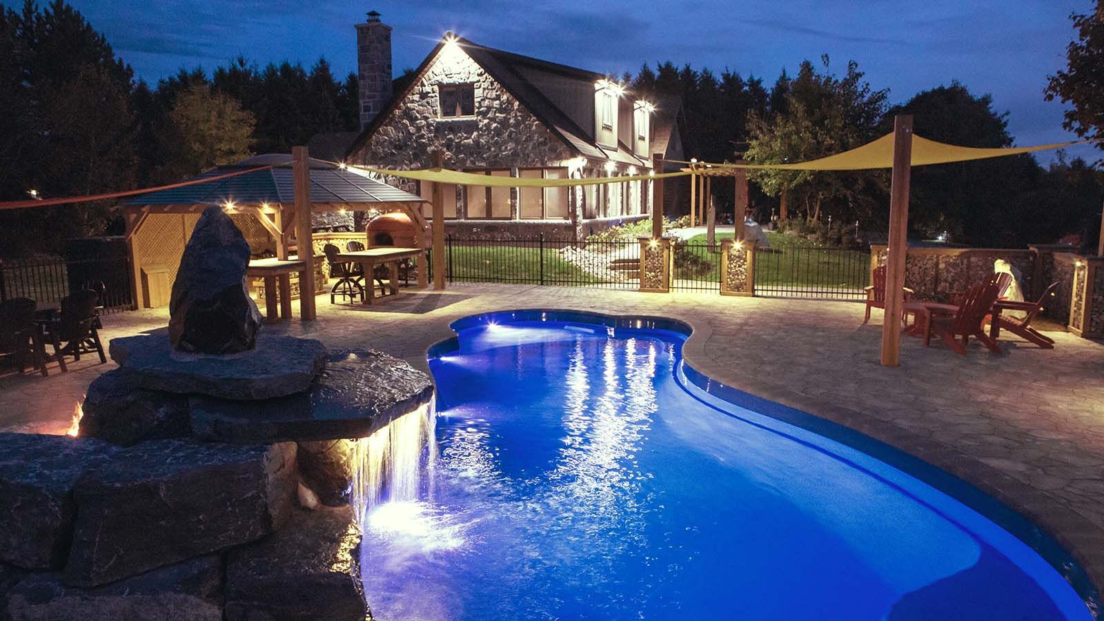 A large swimming pool is lit up at night in front of a house