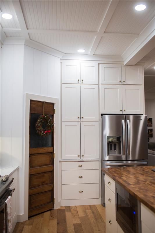 A kitchen with white cabinets , a stainless steel refrigerator and a wooden door.