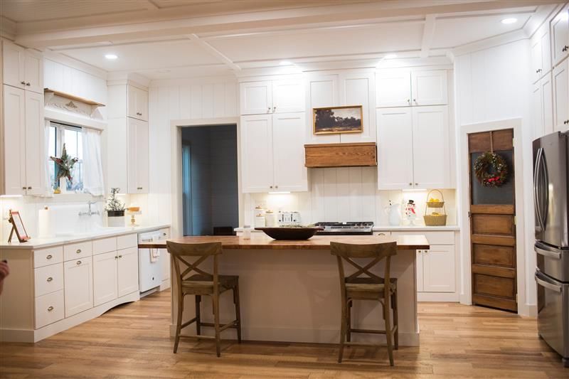 A kitchen with white cabinets , wooden floors , stainless steel appliances and a large island.