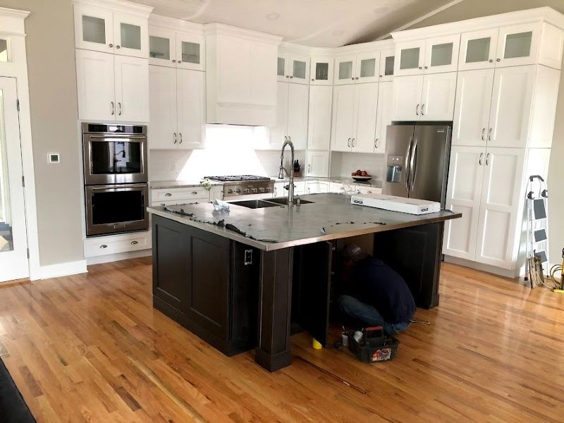 A man is kneeling under a kitchen island in a kitchen.