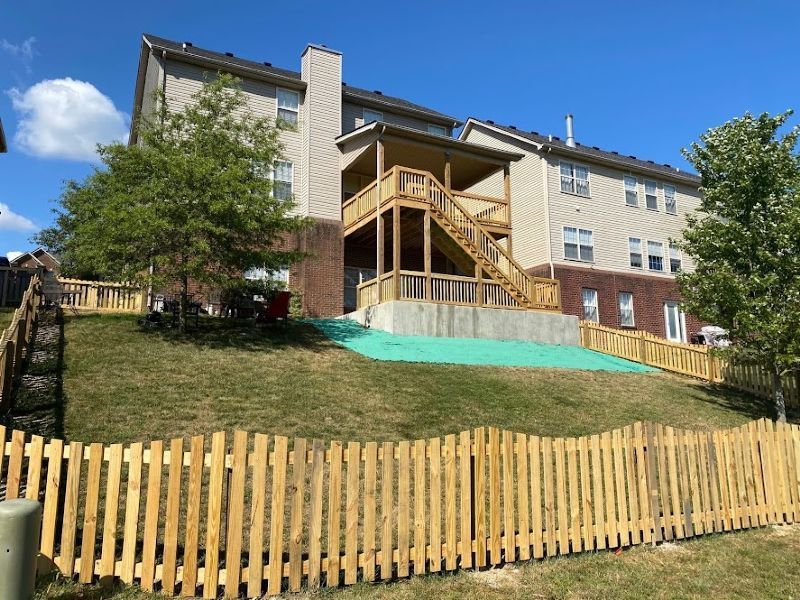 A large house with a wooden deck and stairs behind a wooden fence.