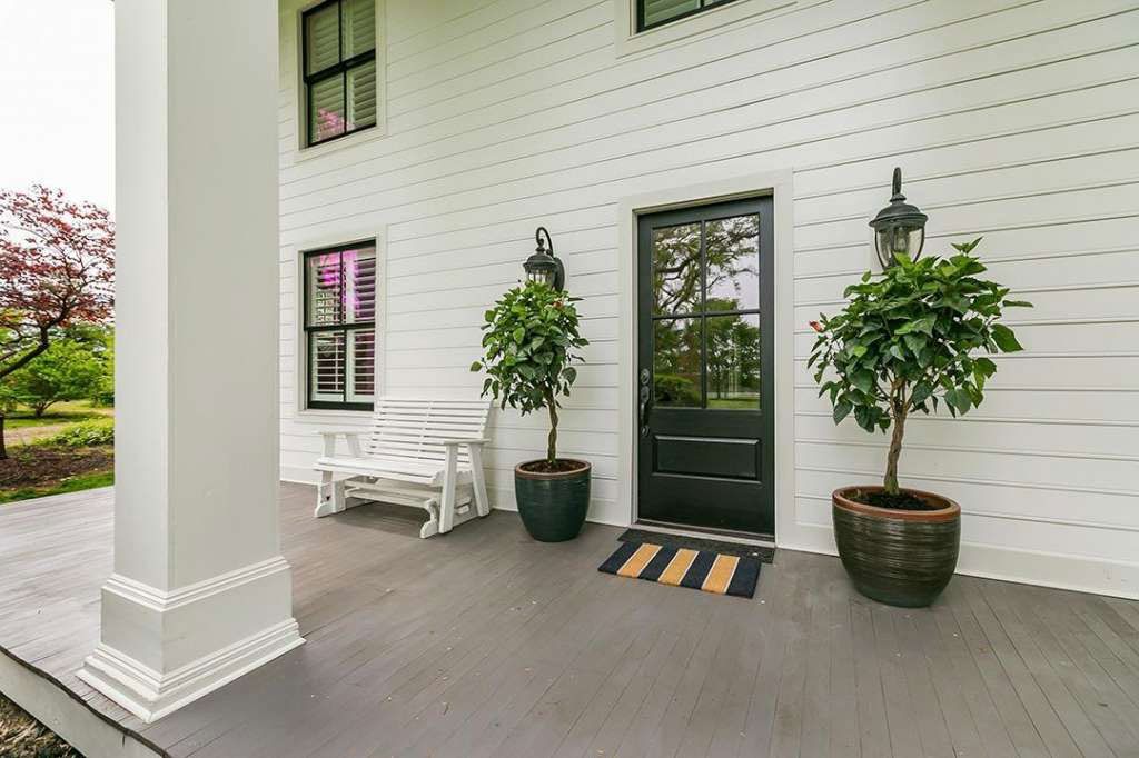 A large white house with a porch with potted plants and a bench