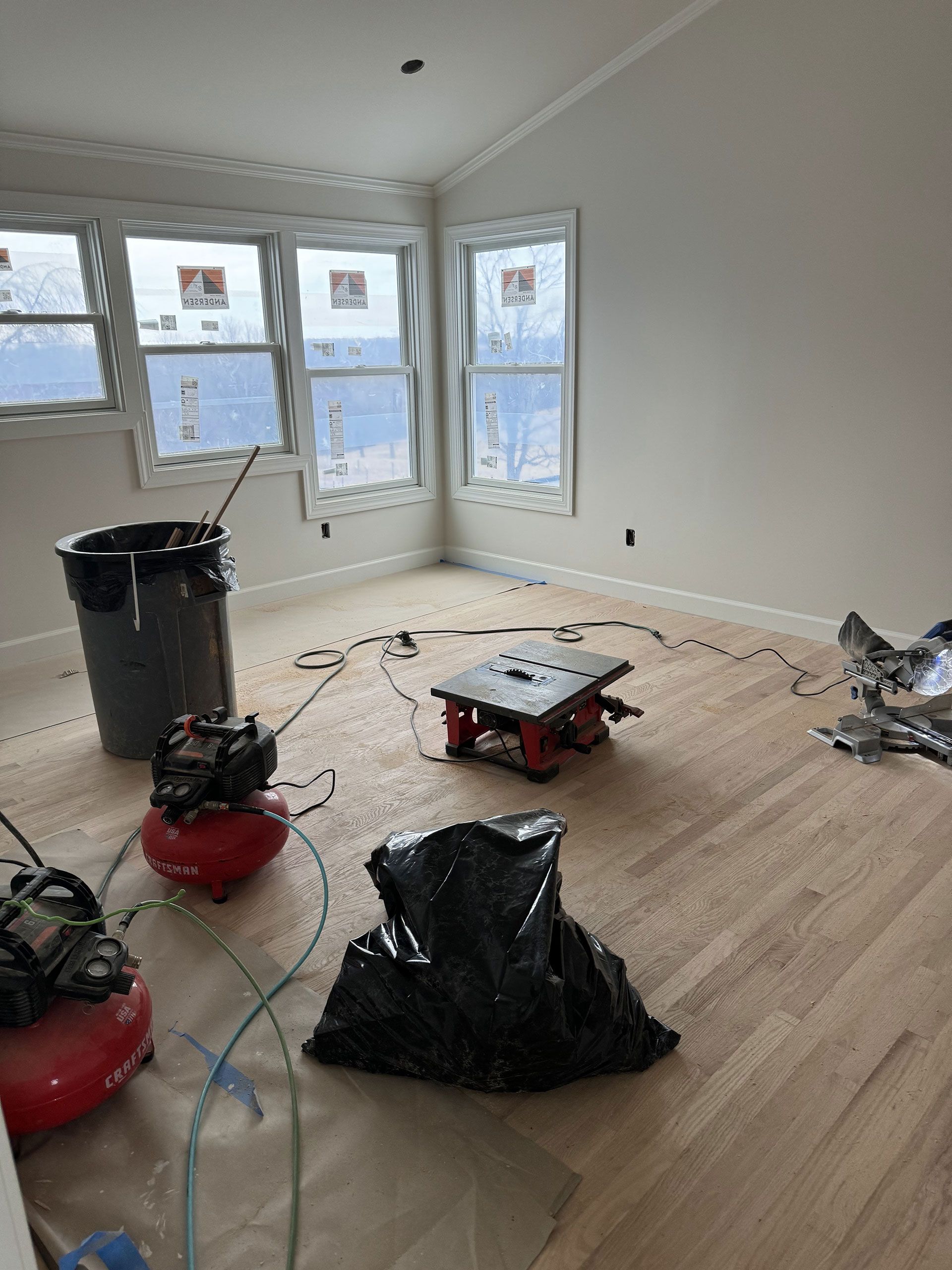 A room with hardwood floors and two air compressors on the floor.