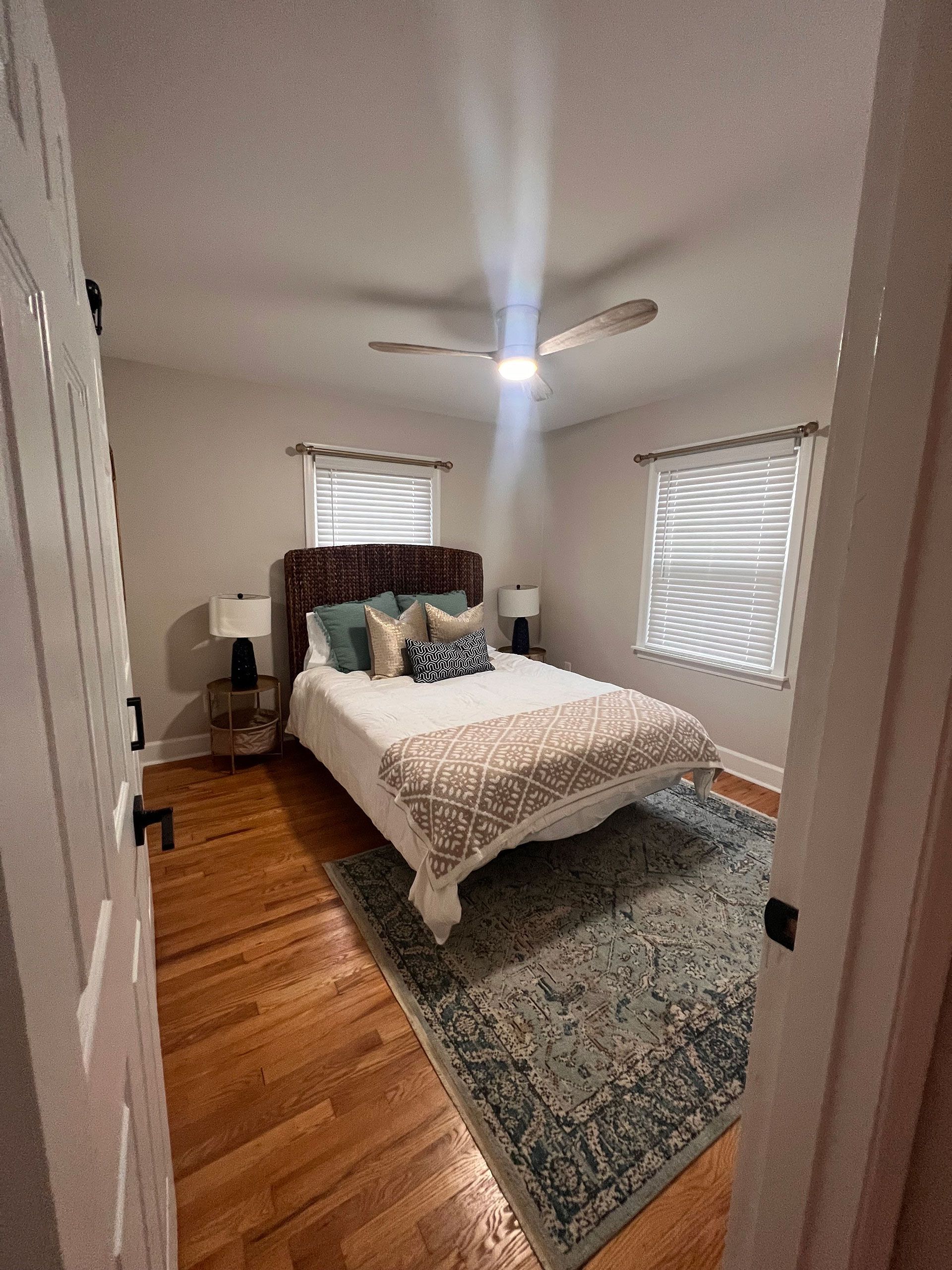 A bedroom with hardwood floors, a bed, a rug and a ceiling fan