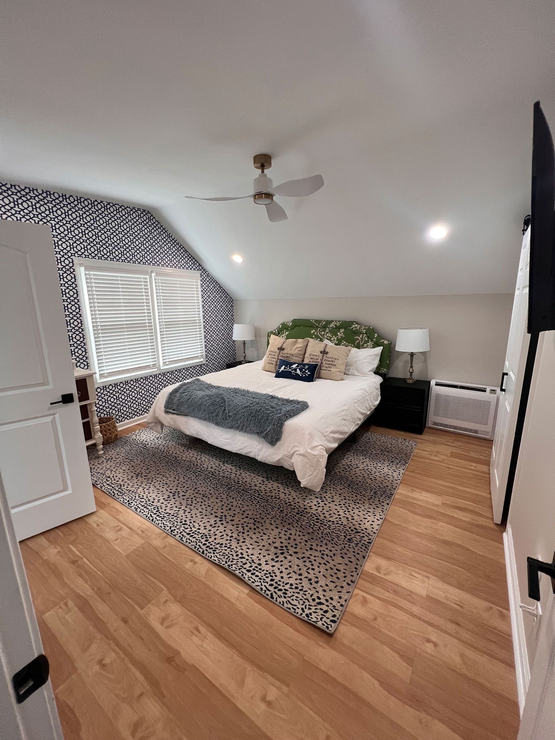 A bedroom with a bed, rug, ceiling fan and window