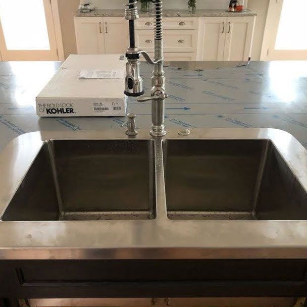 A stainless steel kitchen sink with a kohler box in the background