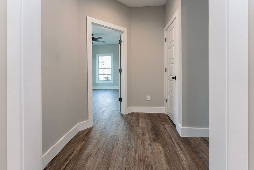 A hallway in a house with hardwood floors and a window.