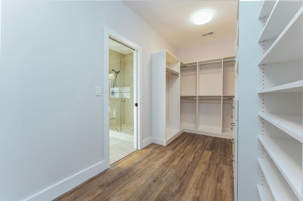 A walk in closet with hardwood floors and white shelves in a house