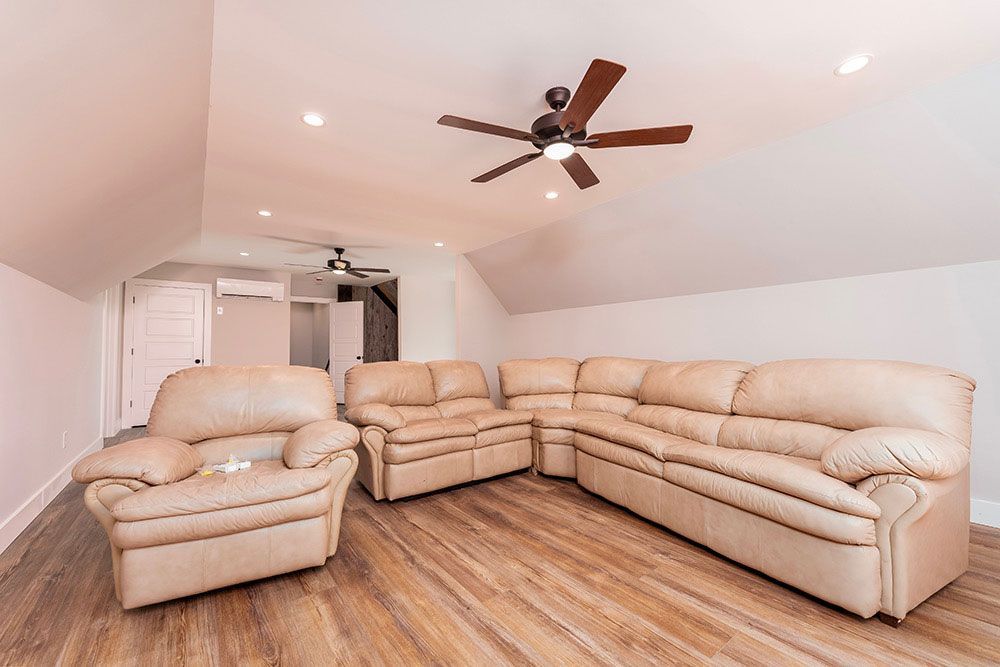 A living room with a sectional couch and two chairs and a ceiling fan