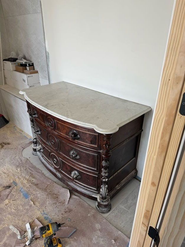 A wooden dresser with a marble top is sitting on the floor in a room