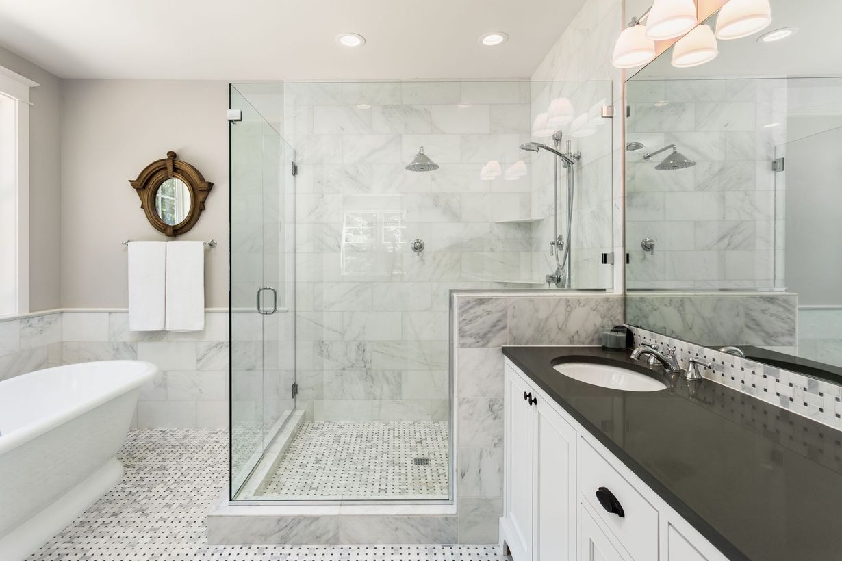 Bright modern bathroom with glass shower, freestanding tub, and black vanity countertop