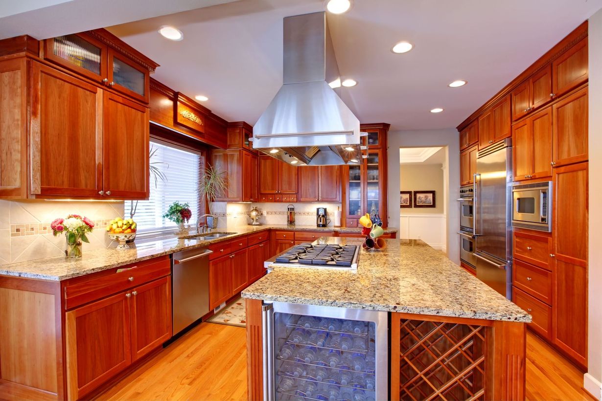 Modern kitchen with cherry wood cabinets, granite island, stainless hood, and warm recessed lighting