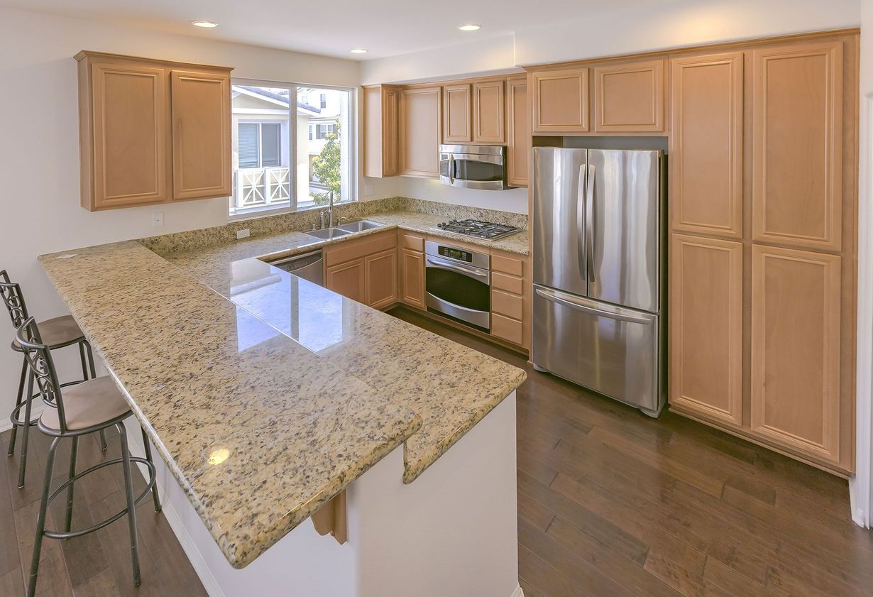 Modern kitchen with granite island, stainless steel appliances, and light wood cabinets