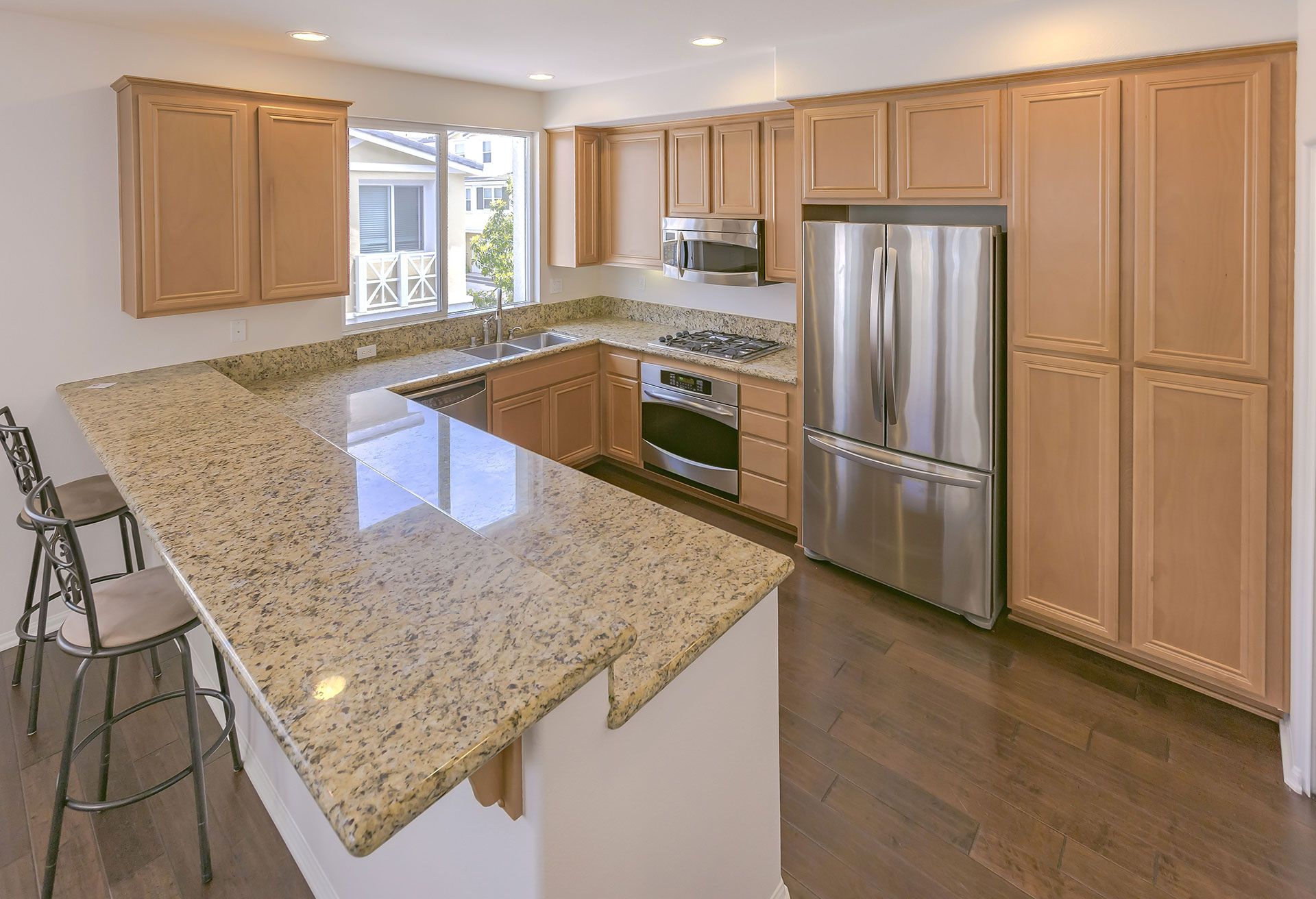 Modern kitchen with granite island, stainless steel appliances, and light wood cabinets