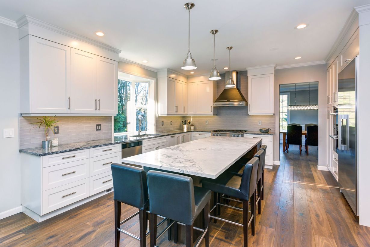Bright modern kitchen with large marble island, white cabinets, pendant lights, and hardwood floors