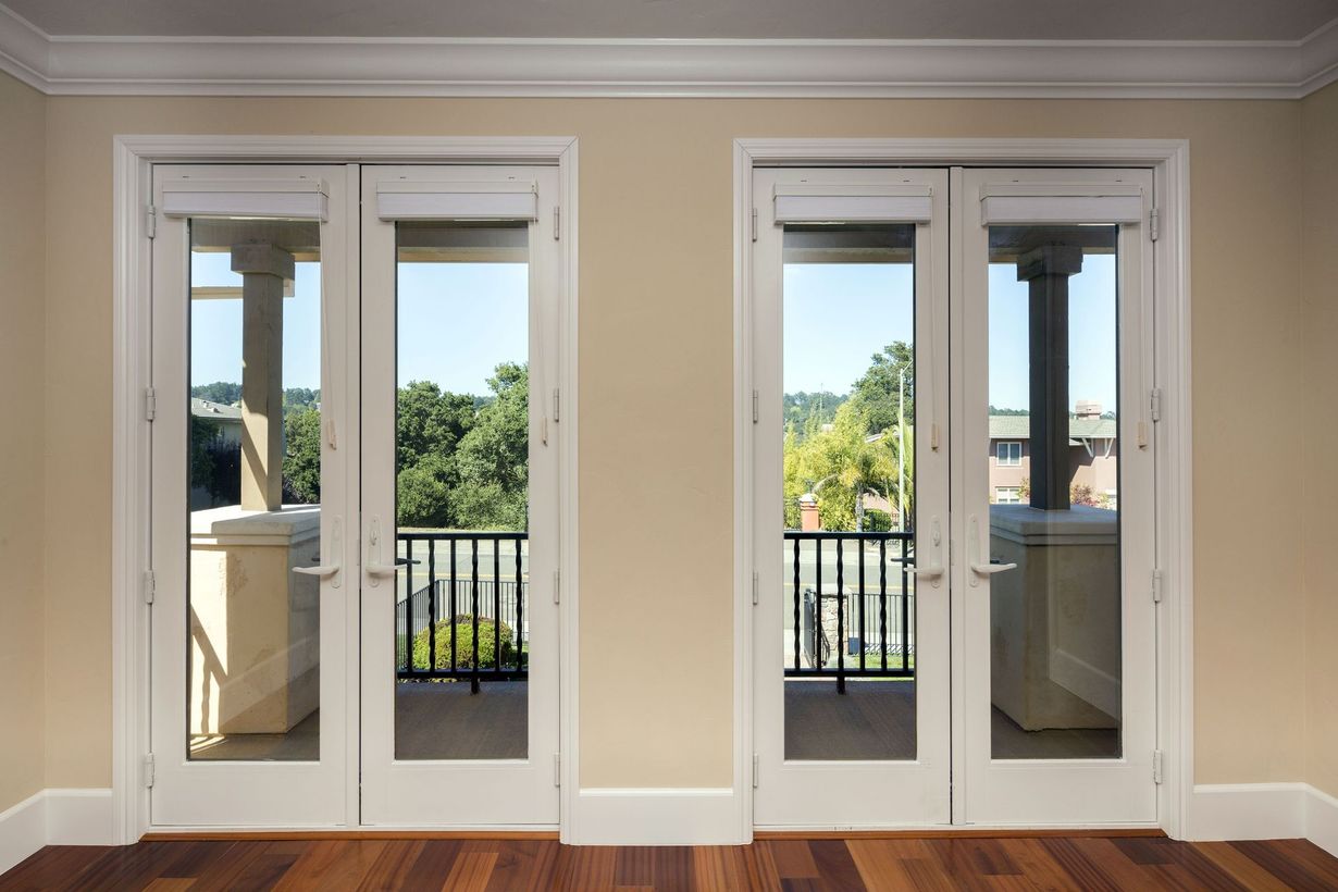 Bright room with two white French doors, balcony railings, and trees outside