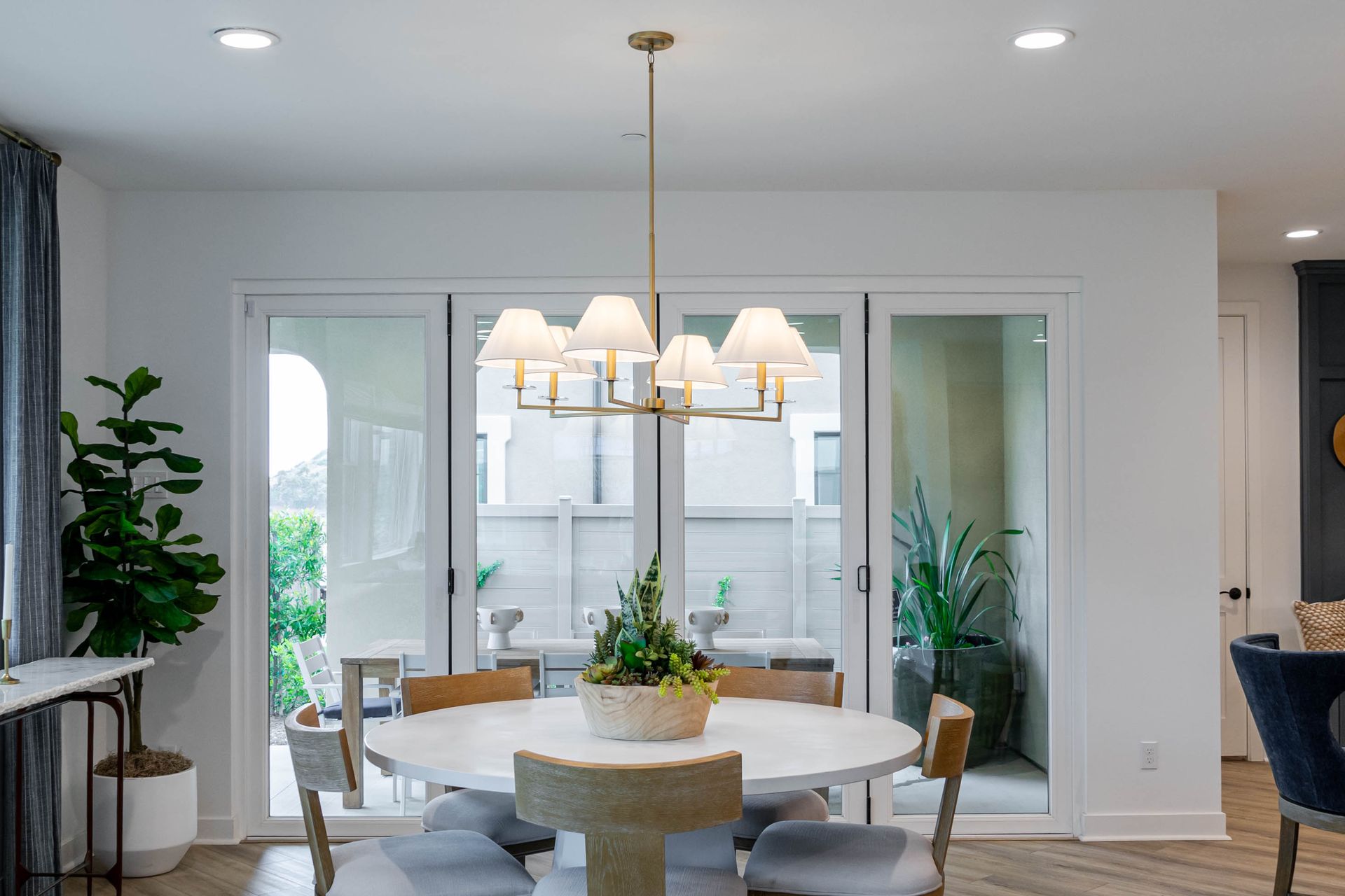 Bright dining room with a round table, beige chairs, chandelier, and sliding glass doors to a patio.