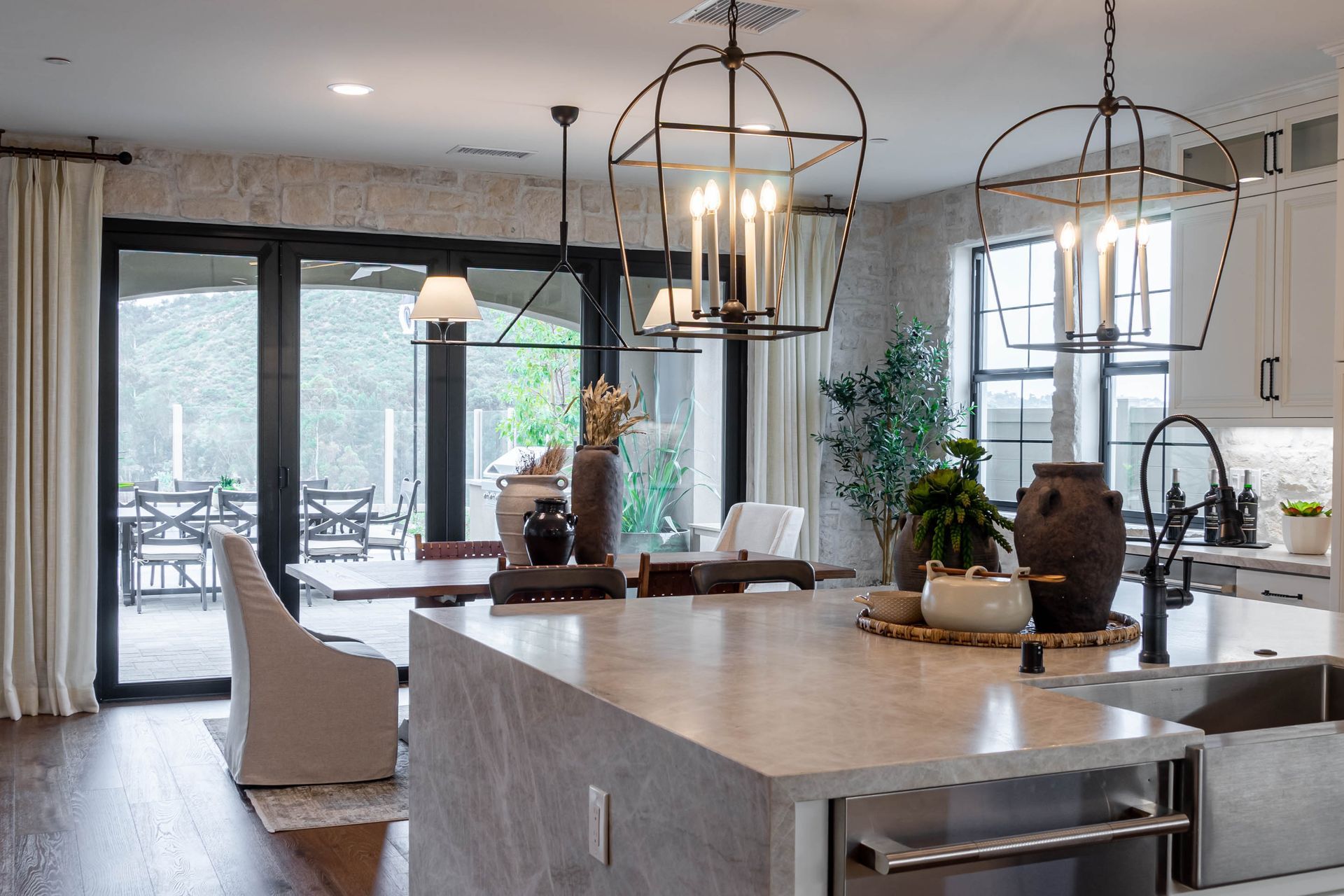 Modern kitchen with island, pendant lights, white cabinets, and large windows opening to a patio