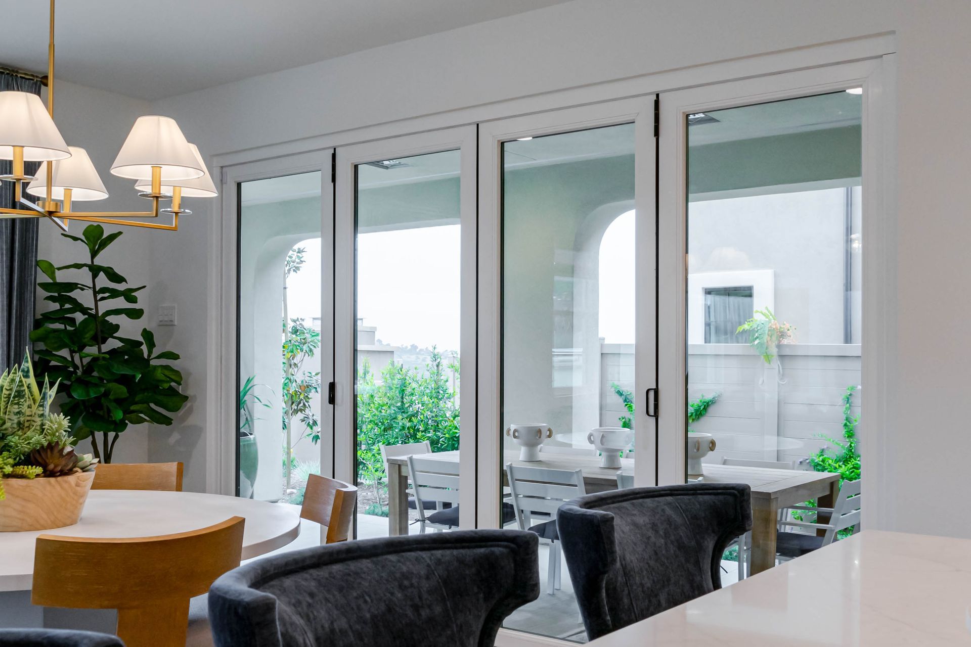 Bright dining room with glass doors opening to a patio and greenery beyond