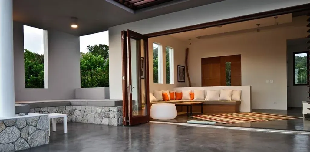 Modern open-air patio with white bench, orange cushions, and stone seating overlooking greenery