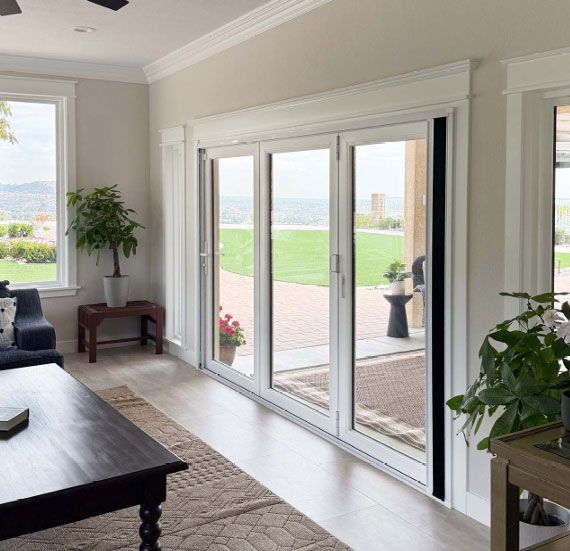 Bright living room with large glass doors opening to a patio and green landscape outside