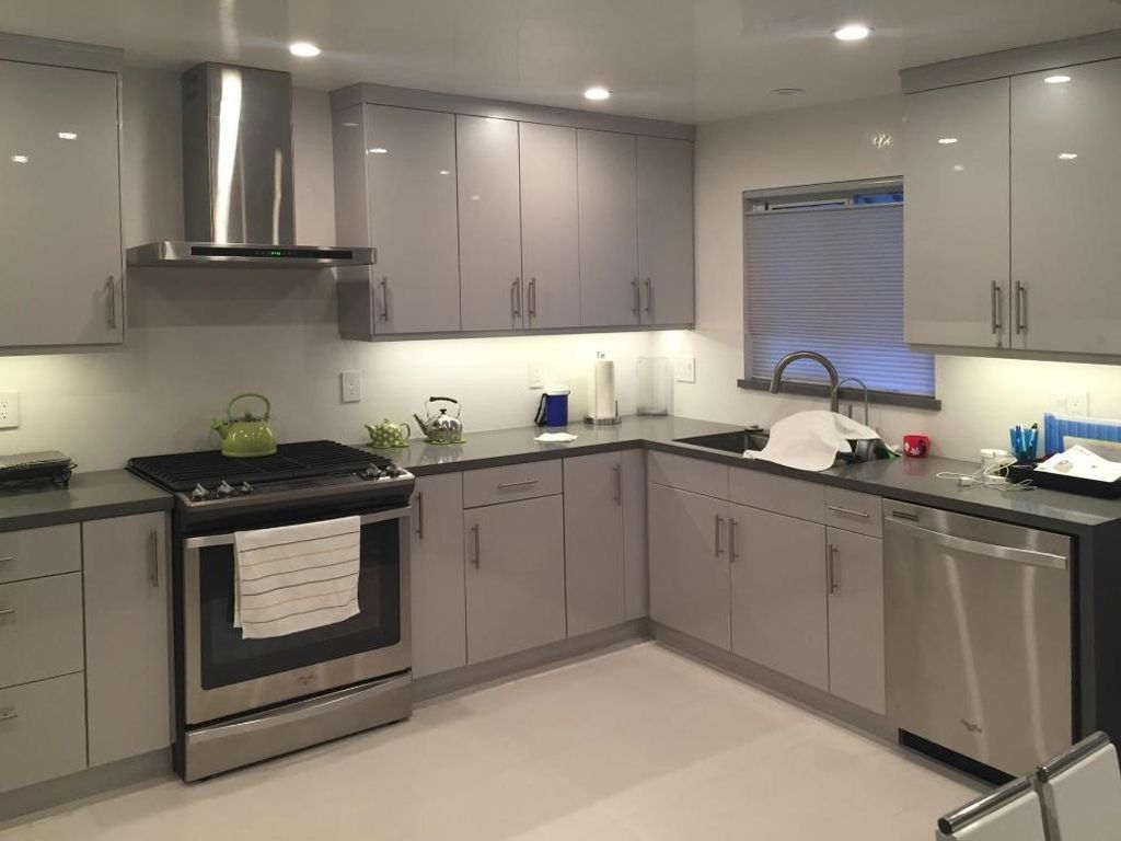 Modern gray kitchen with stainless steel appliances, white counters, and recessed ceiling lights