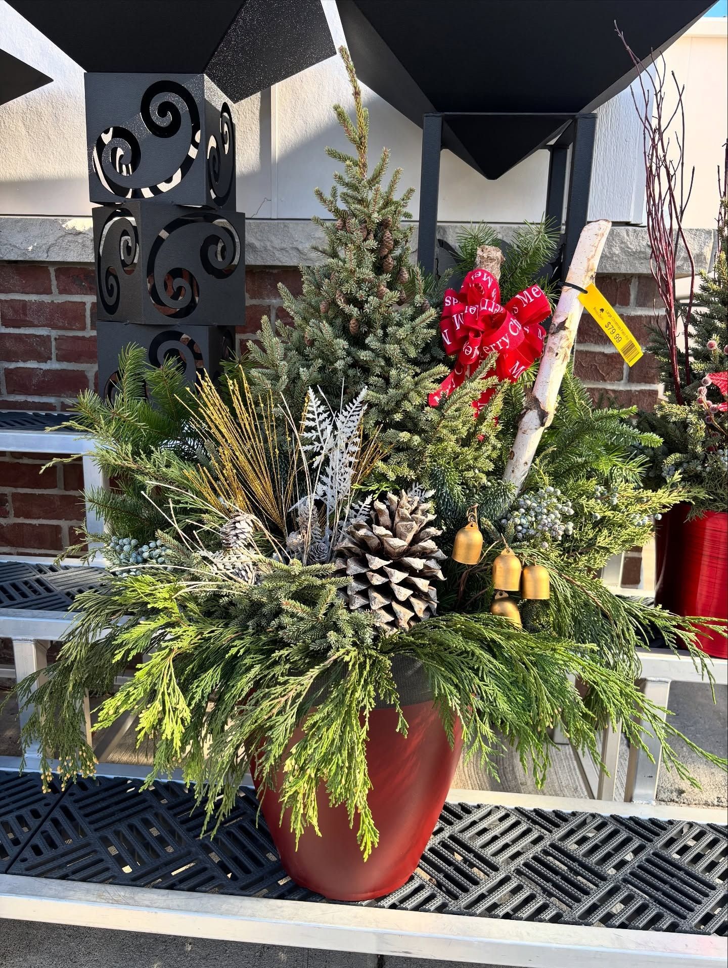 Red pot with Christmas greenery, pinecone, birch branch, red bow, and small bells.
