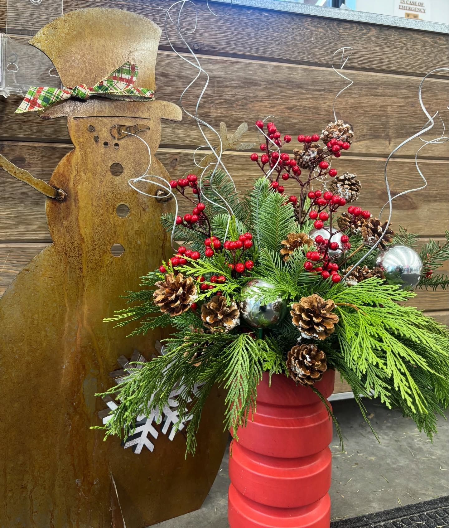 Christmas floral arrangement in a red vase with a snowman cutout backdrop.