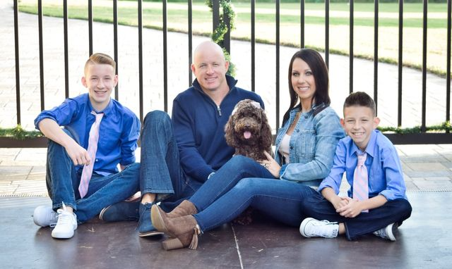 Family sitting outdoors with a small dog in front of a black fence