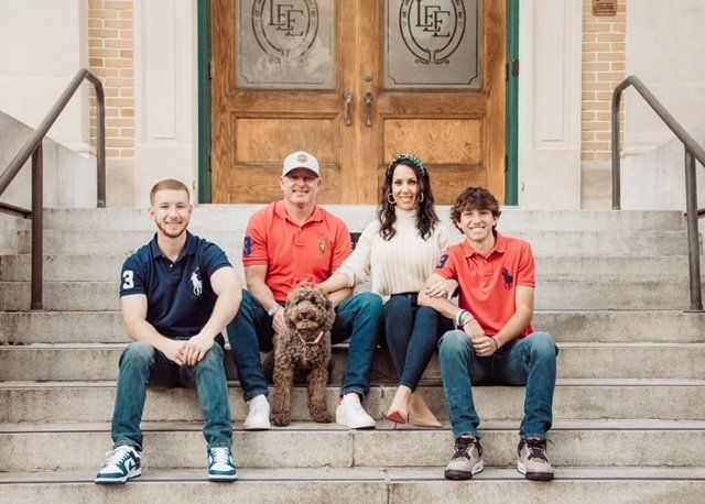 Four people and a brown dog sitting on stone steps in front of wooden doors