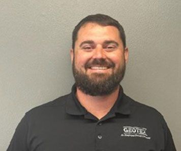 A man with a beard is wearing a black polo shirt and smiling.