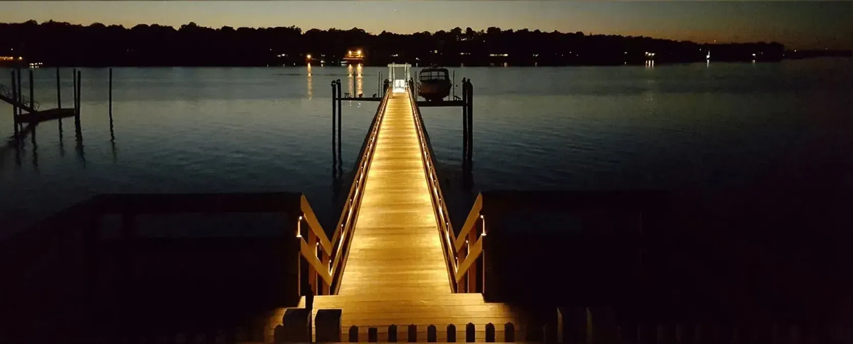 Lit wooden pier extending into dark water at dusk.