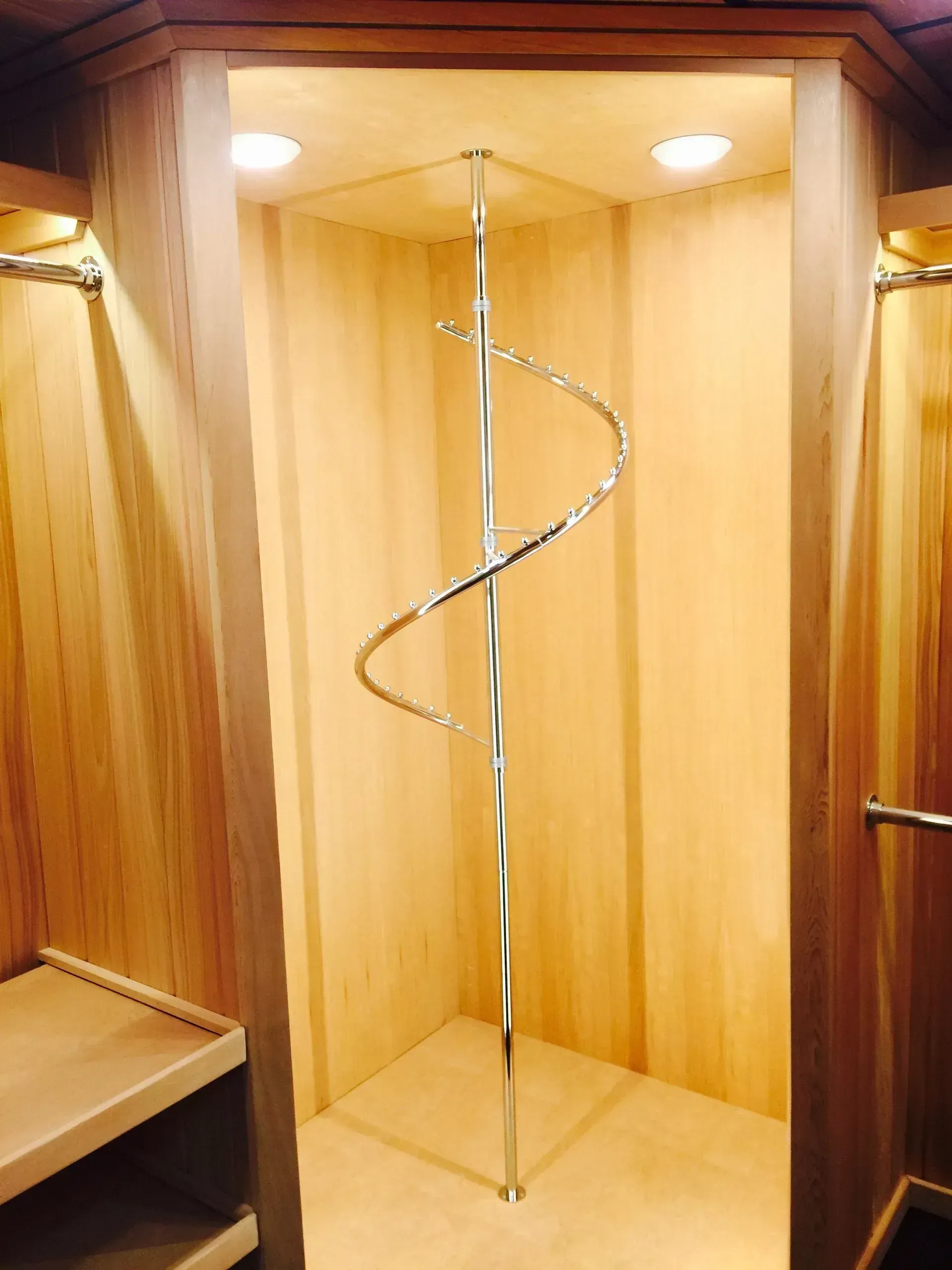 Walk-in closet with cedar walls and a chrome spiral hanging rack. Wooden shelf on the left.