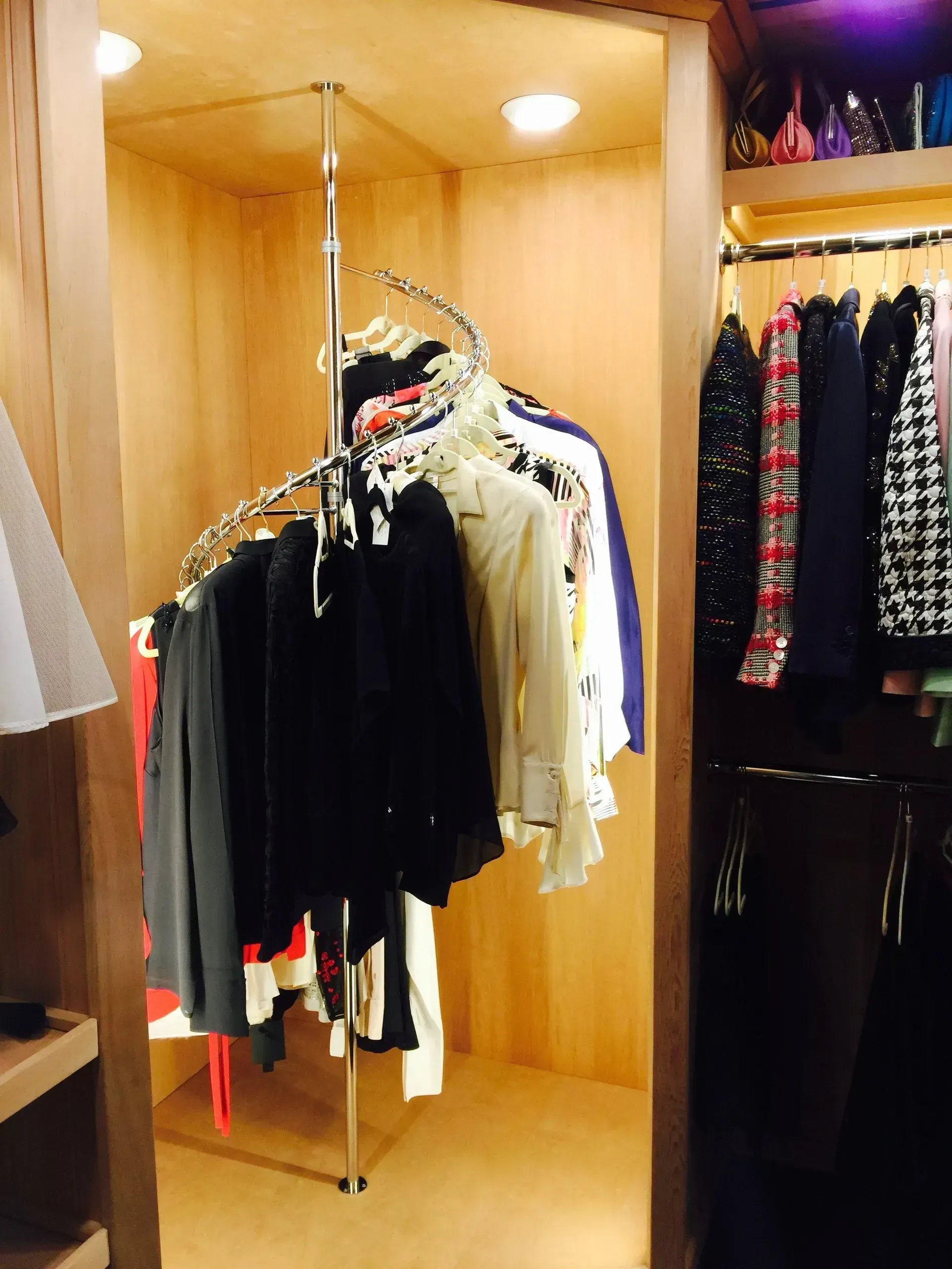 Closet with a spiral clothes rack, and clothing on hangers.  Wooden interior, with a partially visible shelf.