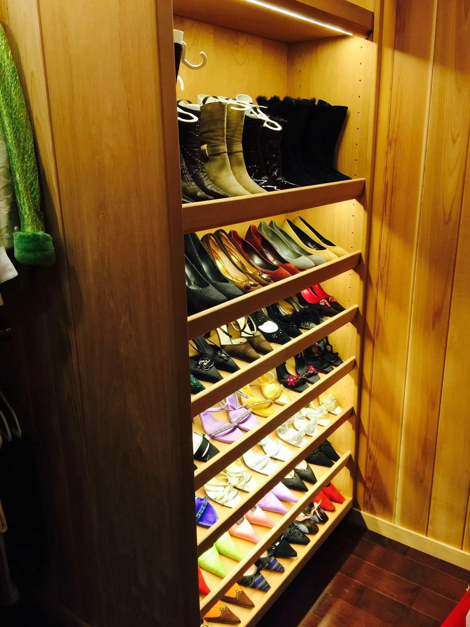 A shoe closet with shelves holding various shoes. The shelves are illuminated by lights.
