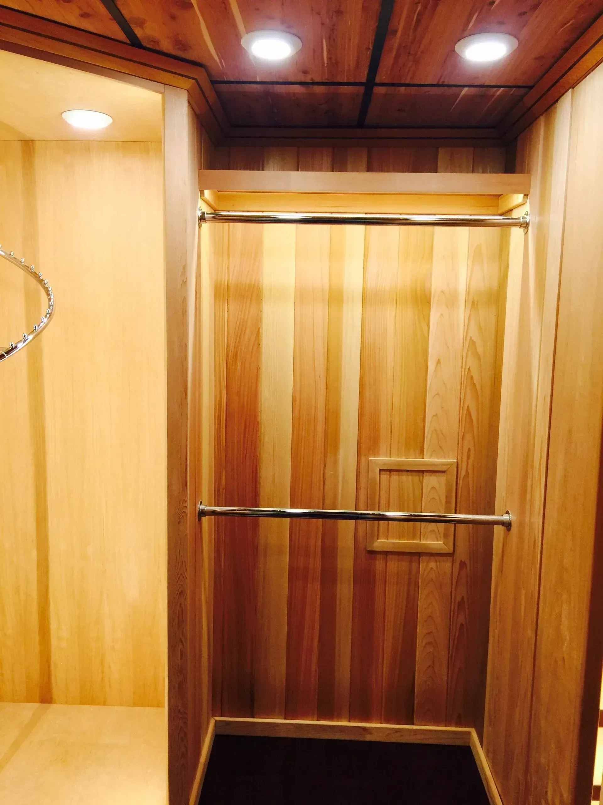 Wooden elevator interior with horizontal grab bars and recessed lighting.
