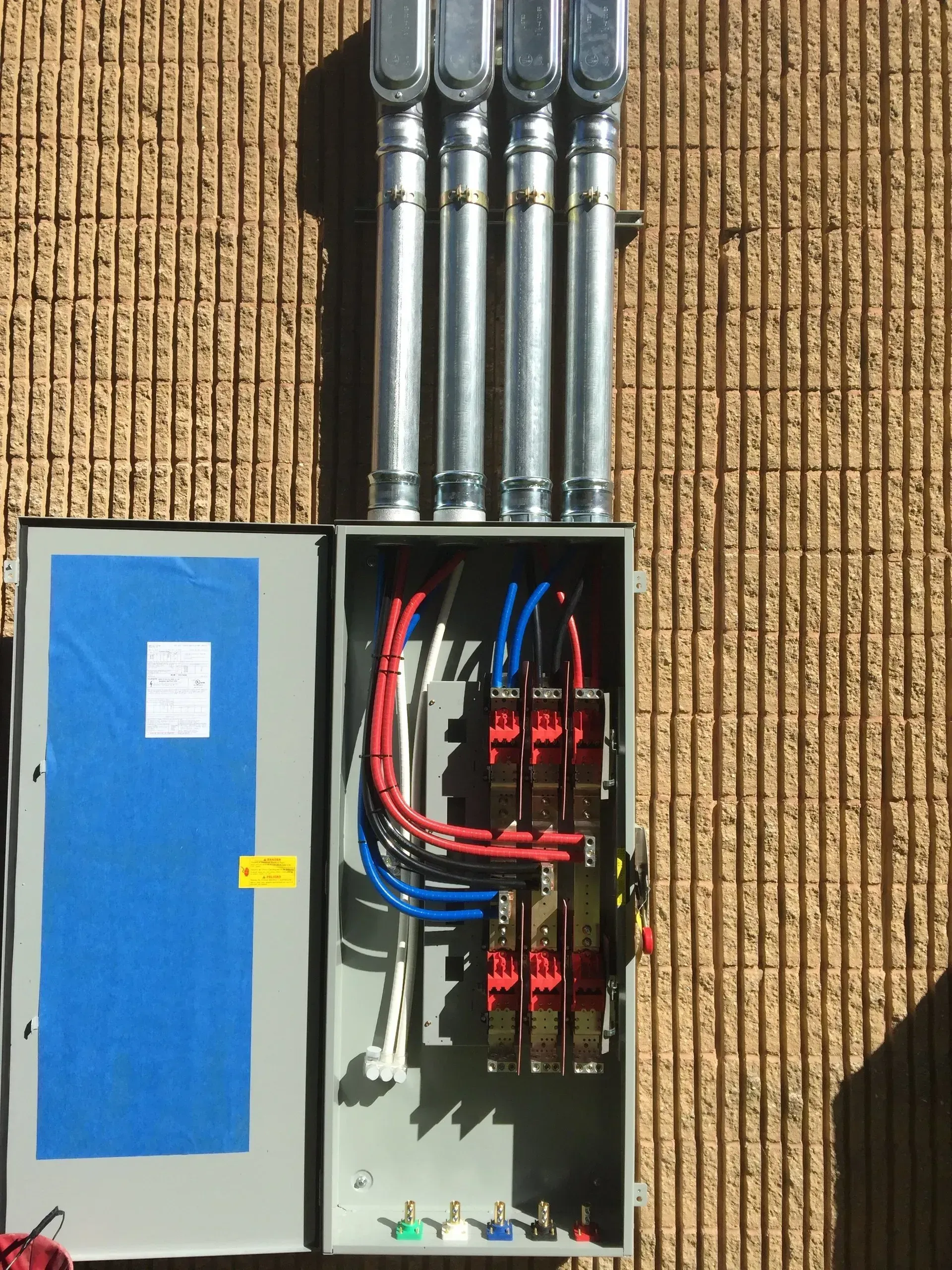 Electrical panel with exposed wiring, metal conduit, mounted on textured brick wall.
