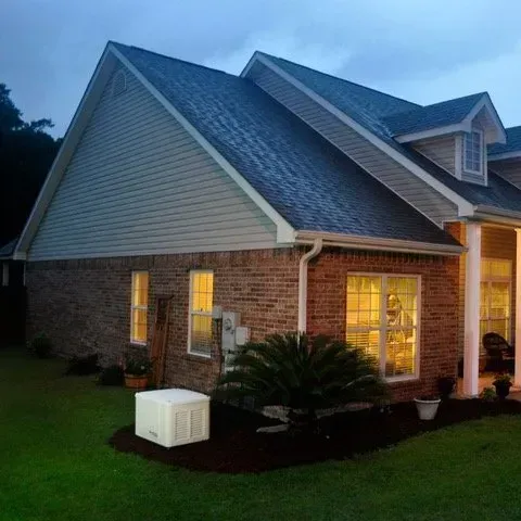 Brick house exterior with a gable roof, windows, and lush green lawn at dusk.