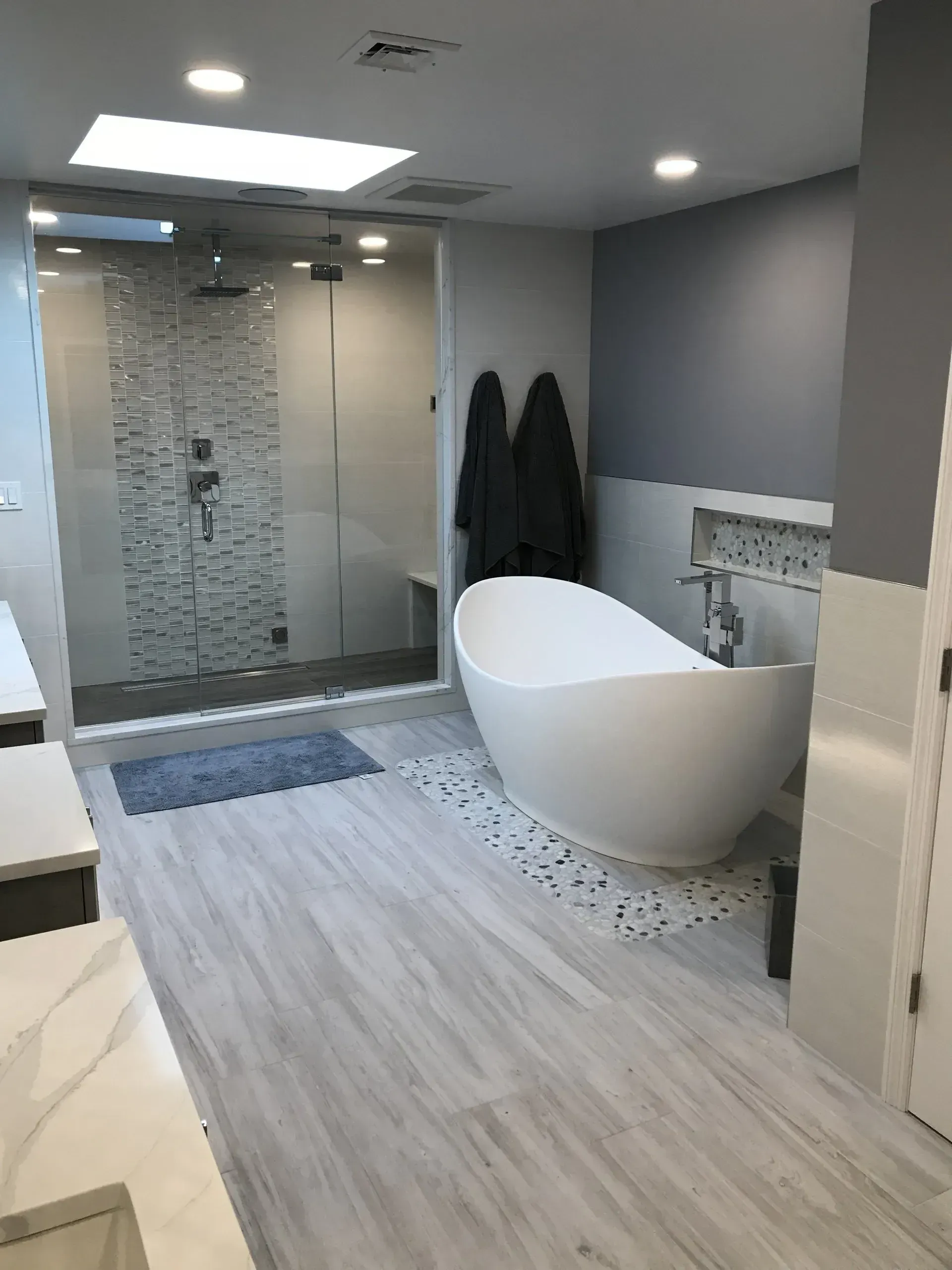 Modern bathroom with white soaking tub, glass shower, light gray walls, and wood-look flooring.
