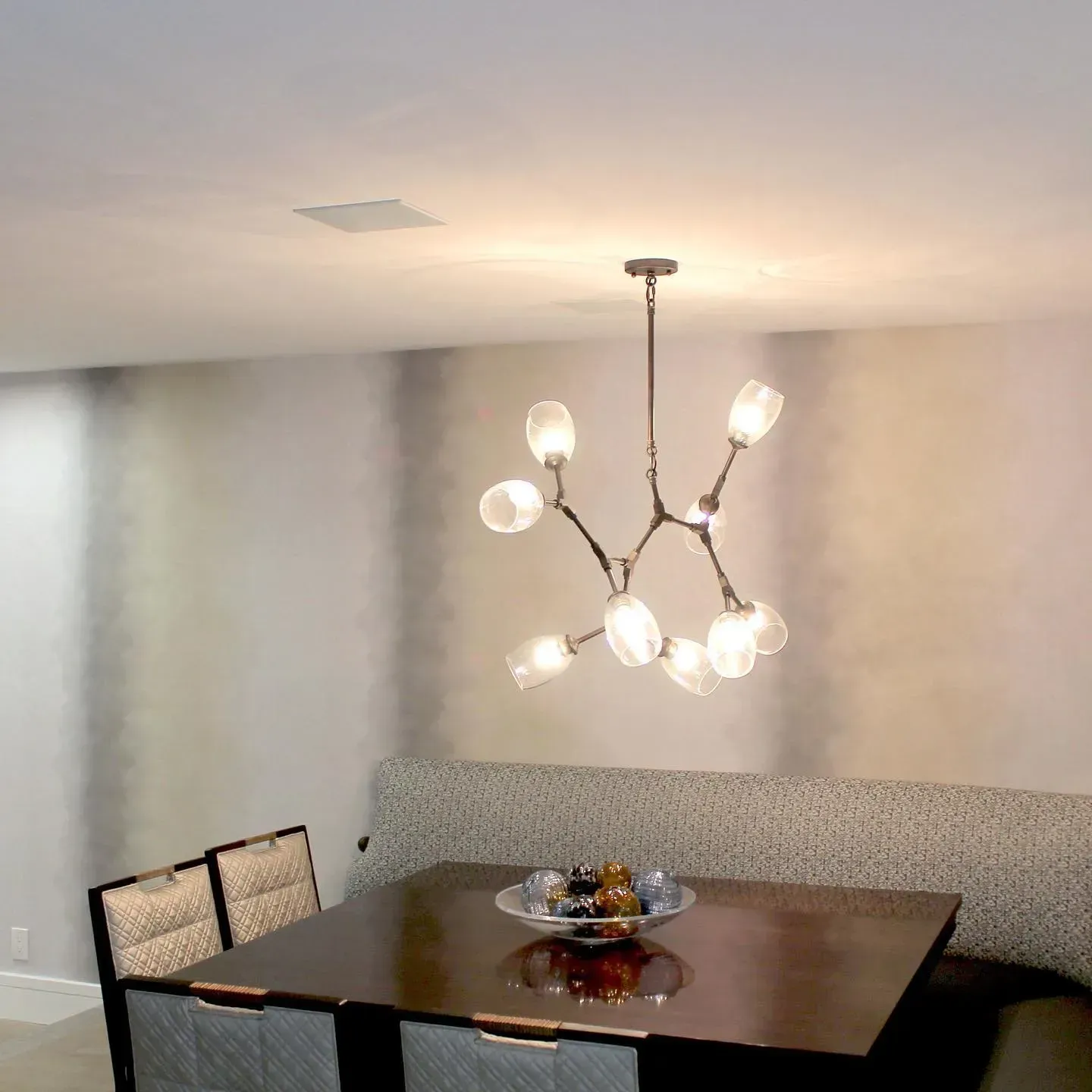 Dining room with chandelier over table, built-in bench, chairs, and patterned wallpaper.