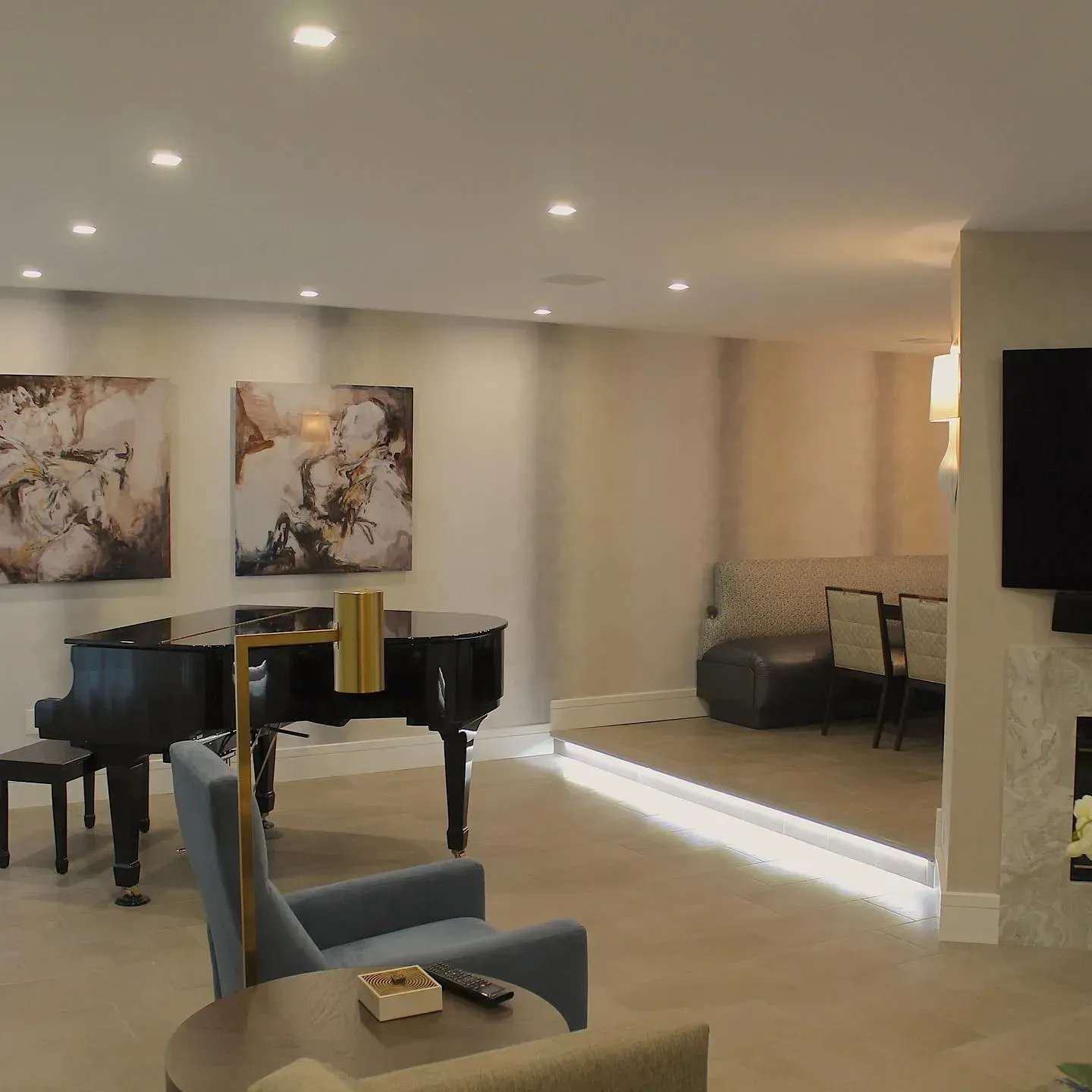 Living room with black piano, artwork, chairs, and raised seating area.