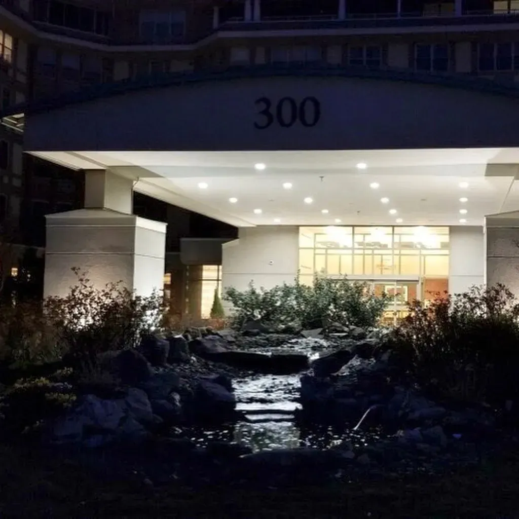 Entrance to building with illuminated "300" sign, water feature in foreground.
