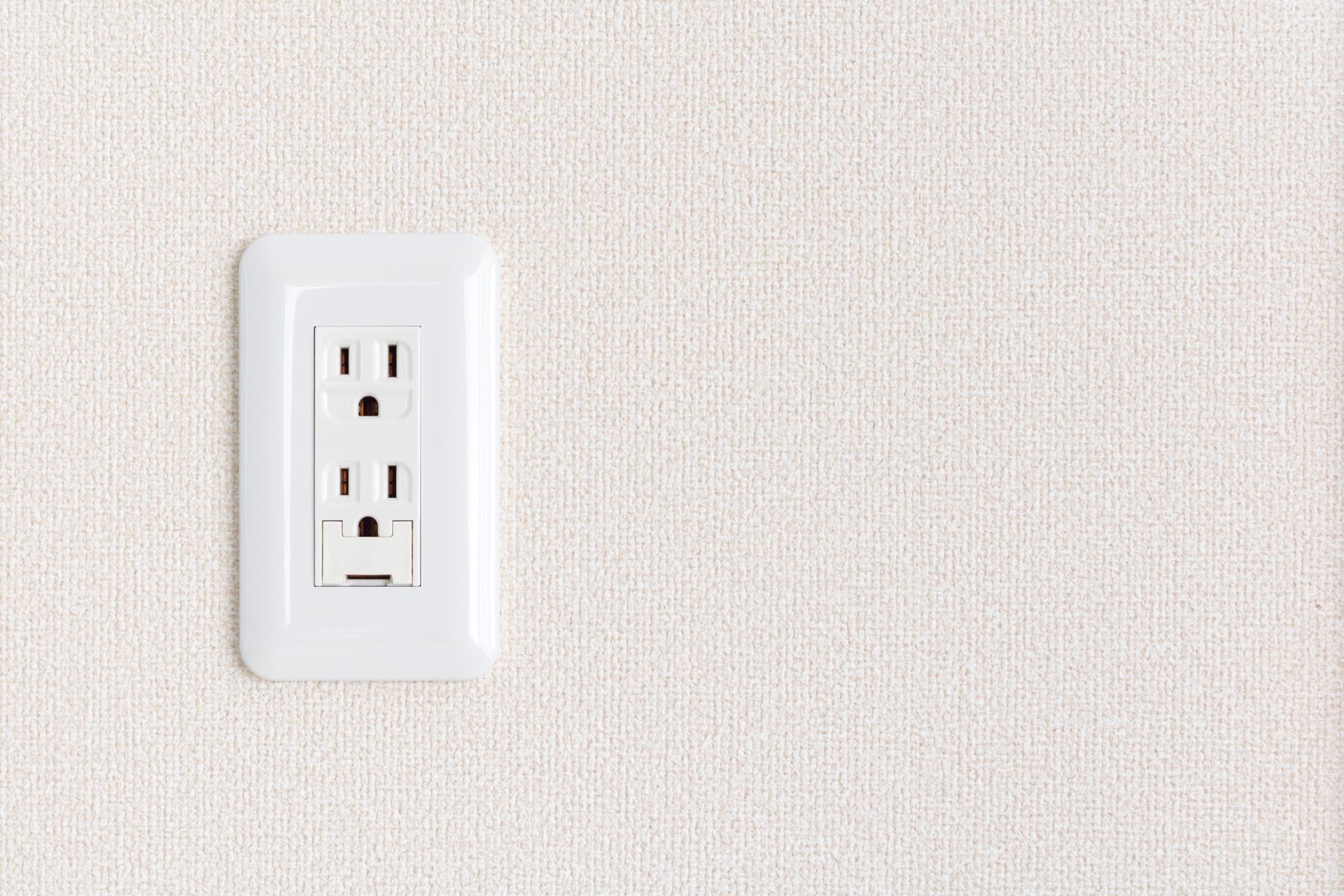 White electrical outlet on textured off-white wall.