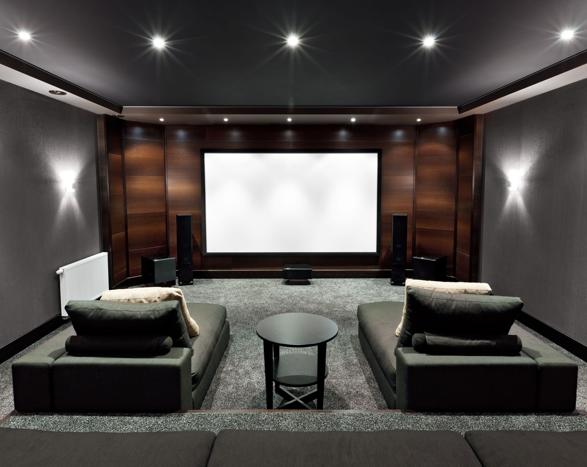 Home theater with a large screen, dark walls, couches, and speakers.