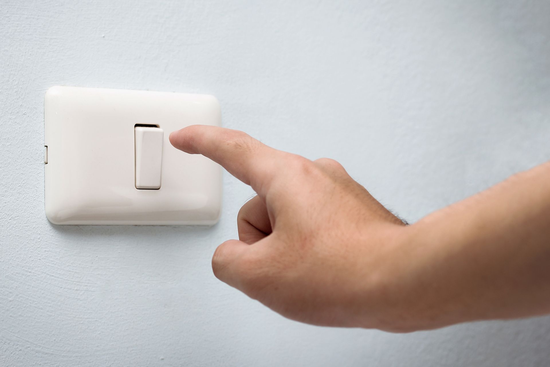 Hand pressing a light switch on a white wall.