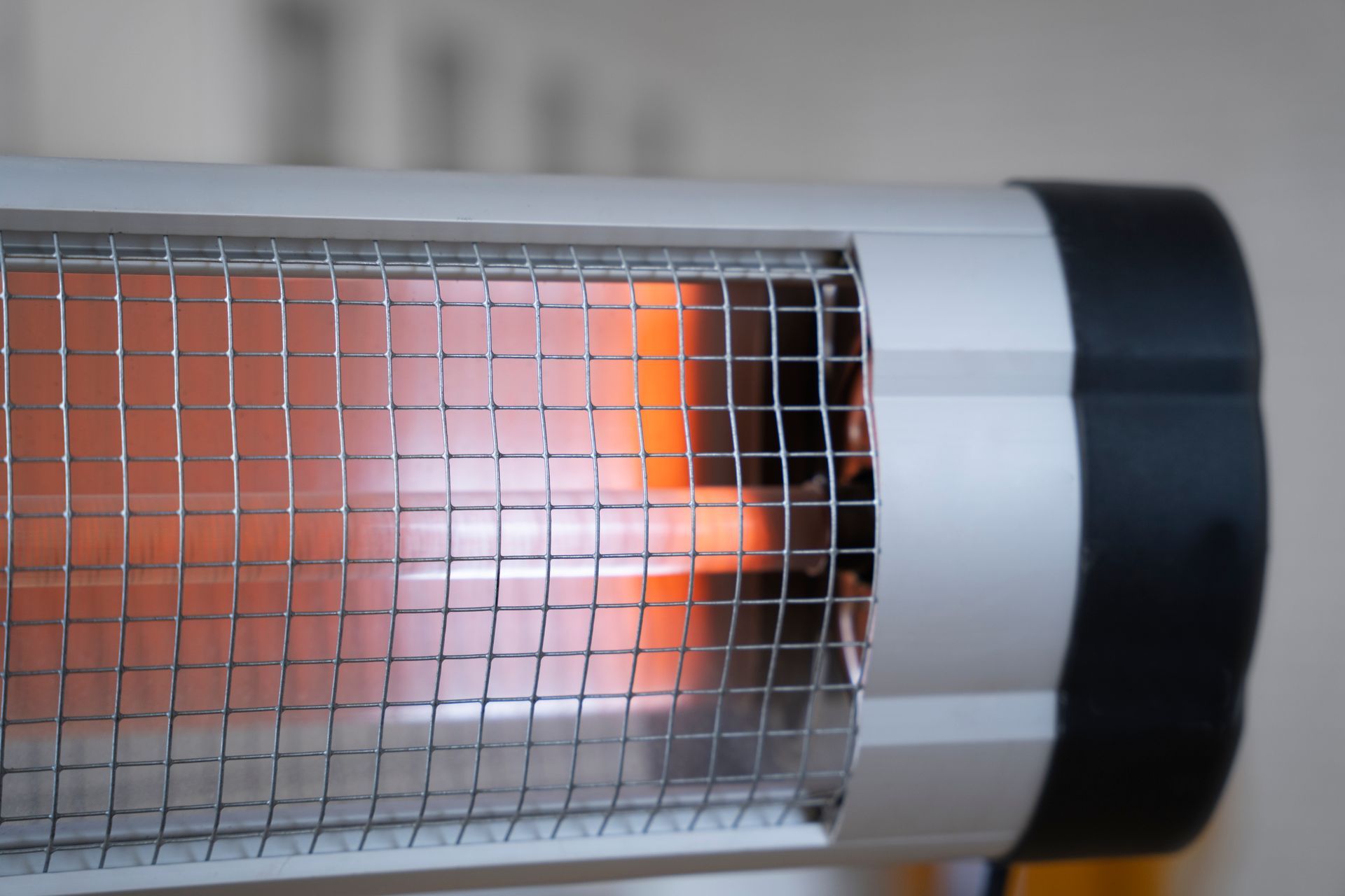 Close-up of a silver electric heater with a glowing orange heating element behind a wire safety grill.