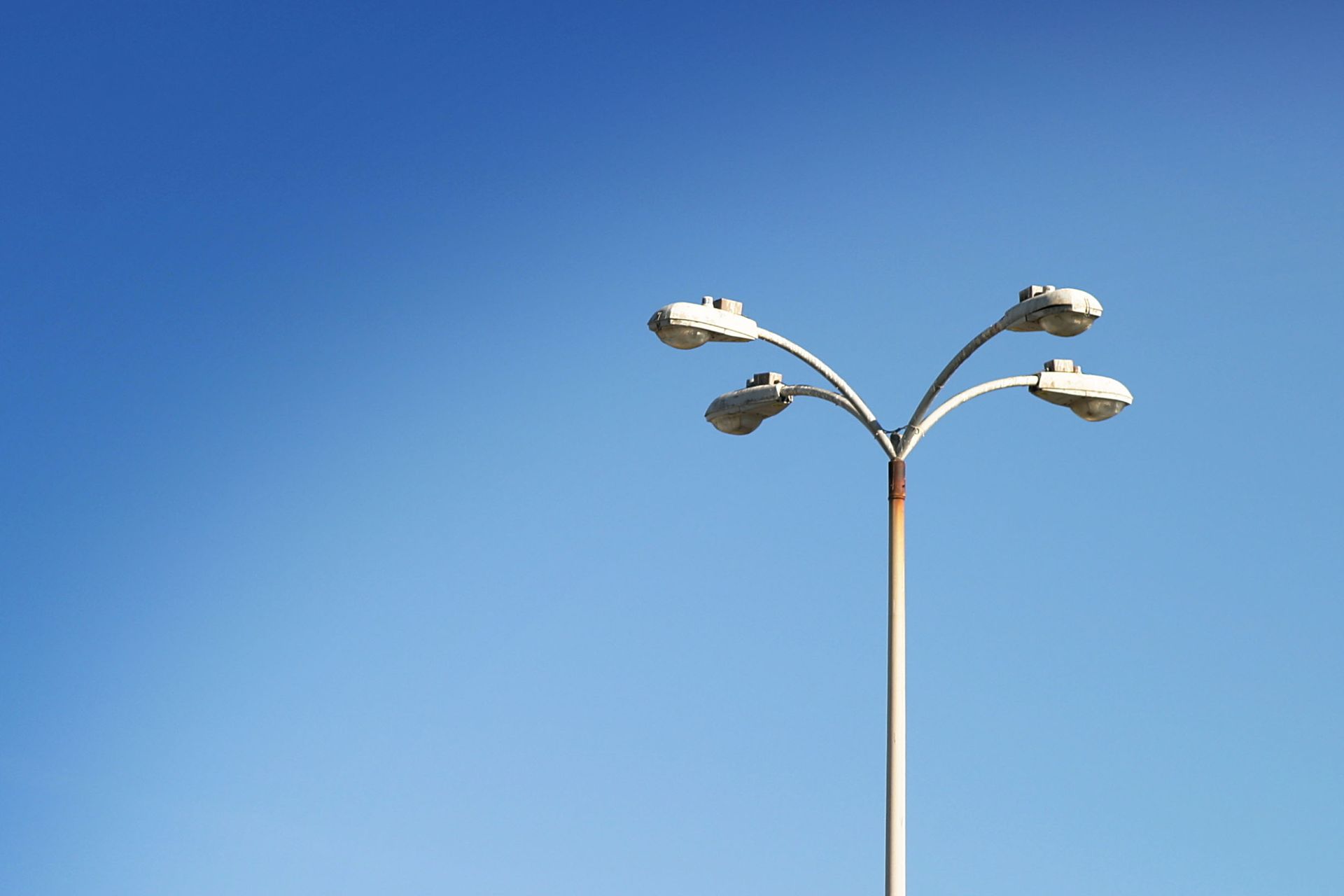 Street lamp with four lights against a bright blue sky.
