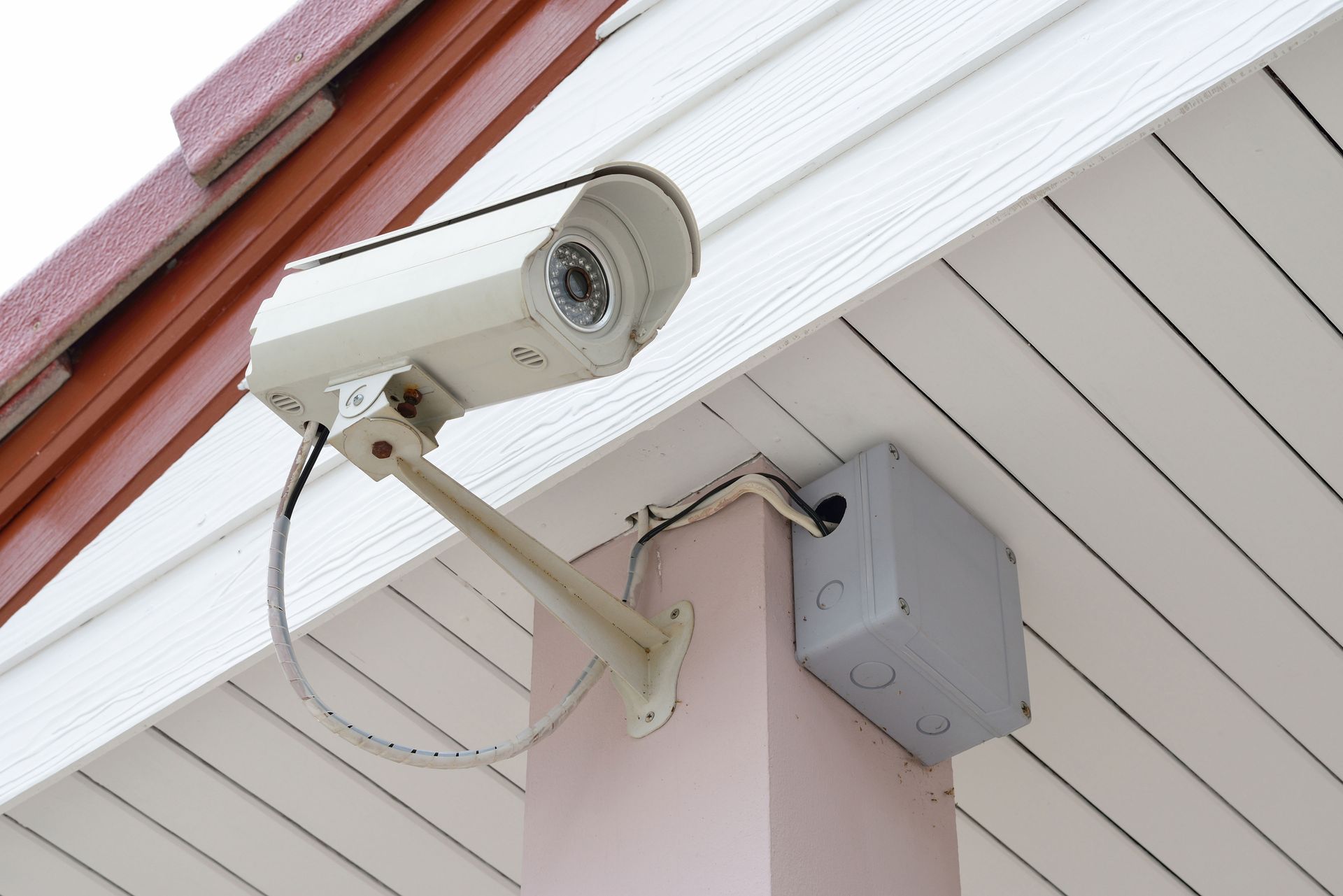 Security camera mounted on a building's white siding, pointing outwards.