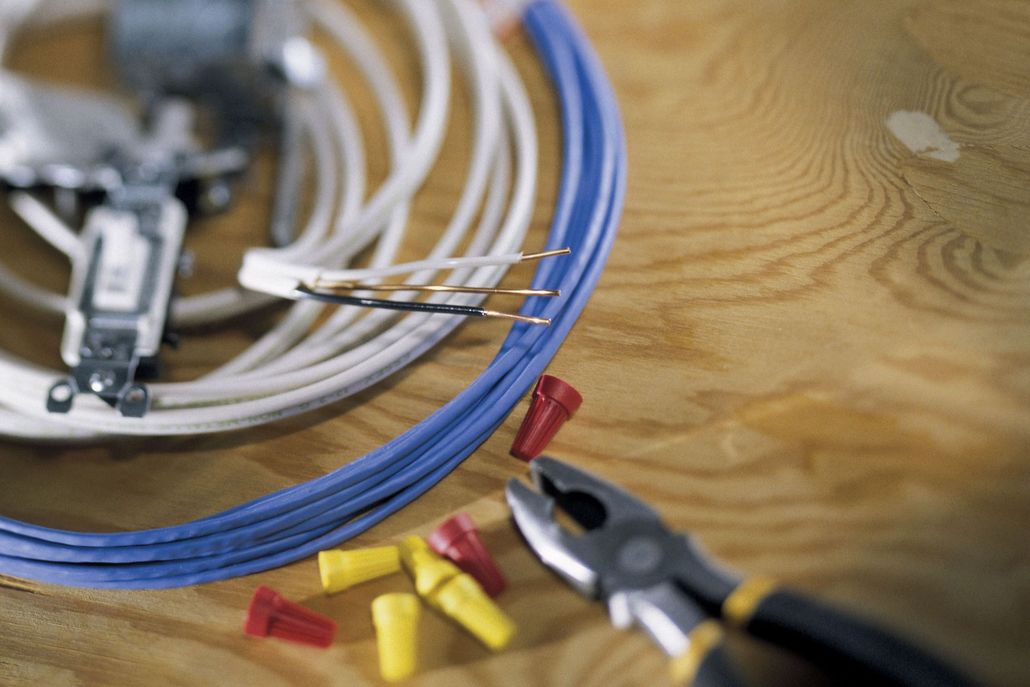 Electrical wiring components including wires, wire connectors, and pliers on wood.