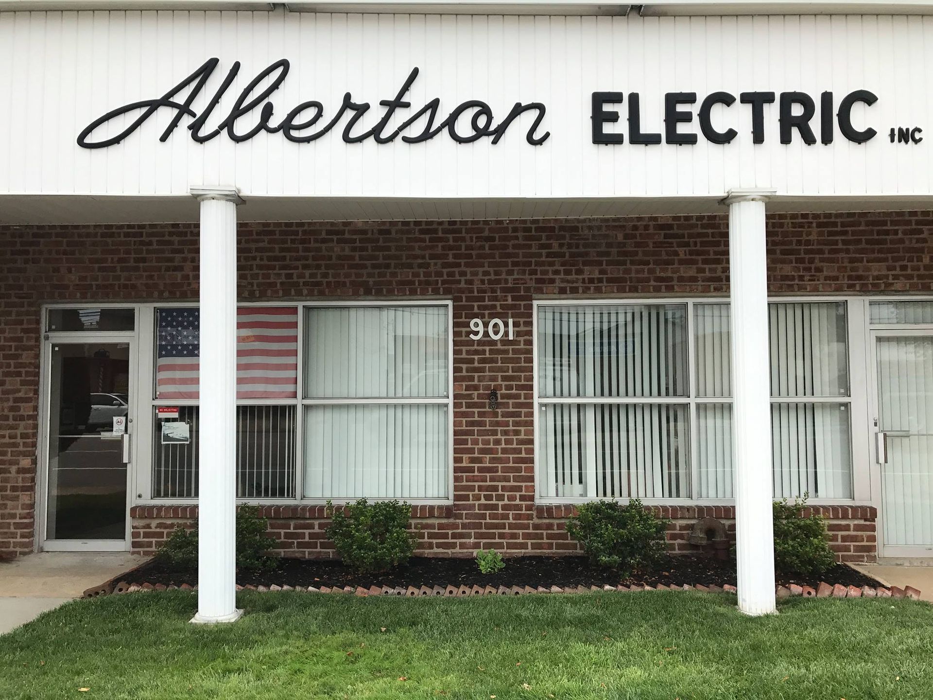 Albertson Electric Inc. storefront with brick facade, white trim, and a U.S. flag visible in a window.